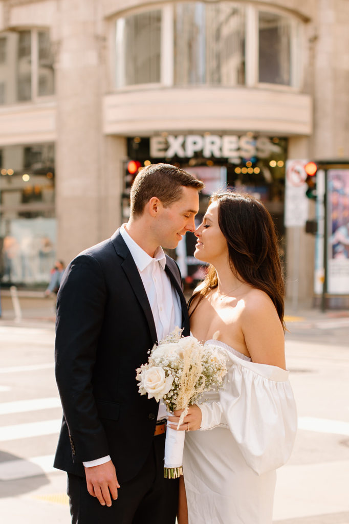 Sydney Jai Photography - San Francisco city elopement, bride and groom almost kissing and holding each other, bride wearing satin off the shoulder wedding dress, groom wearing a classic black suit