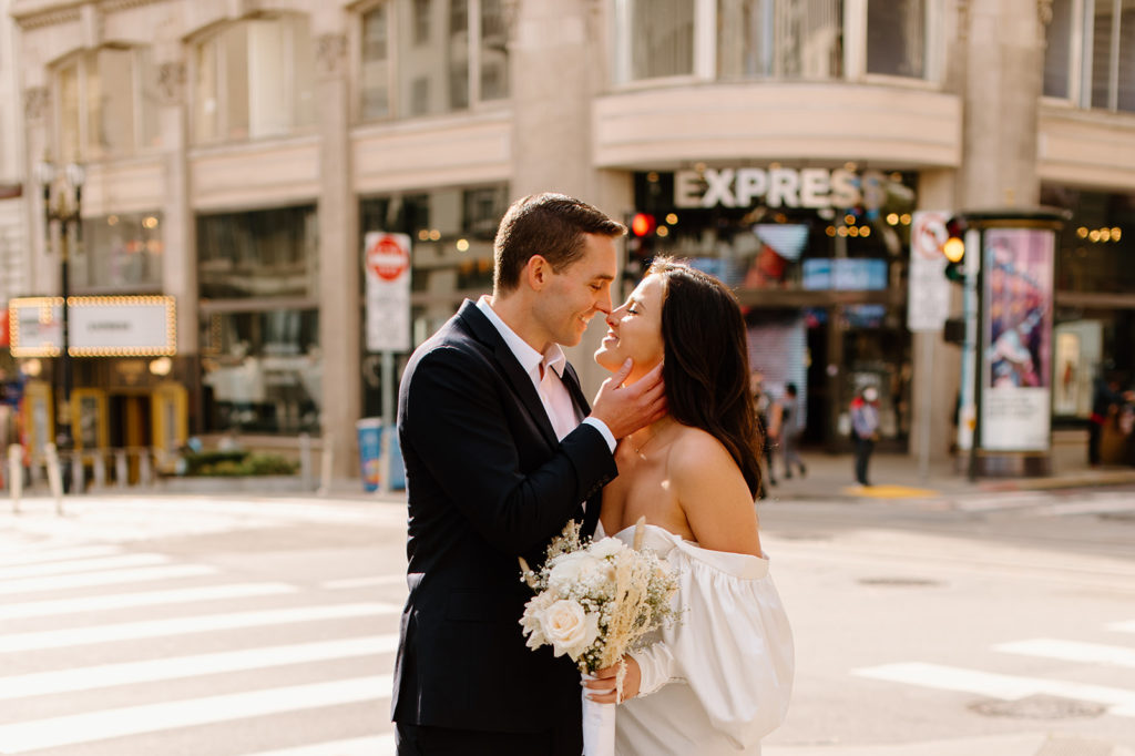Sydney Jai Photography - San Francisco city elopement, bride and groom almost kissing and holding each other, bride wearing satin off the shoulder wedding dress, groom wearing a classic black suit