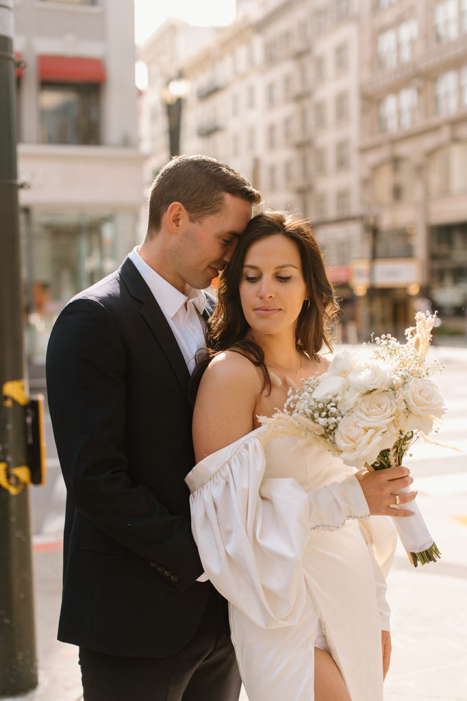 Sydney Jai Photography - San Francisco city elopement, bride and groom holding each other, bride wearing satin off the shoulder wedding dress, groom wearing a classic black suit