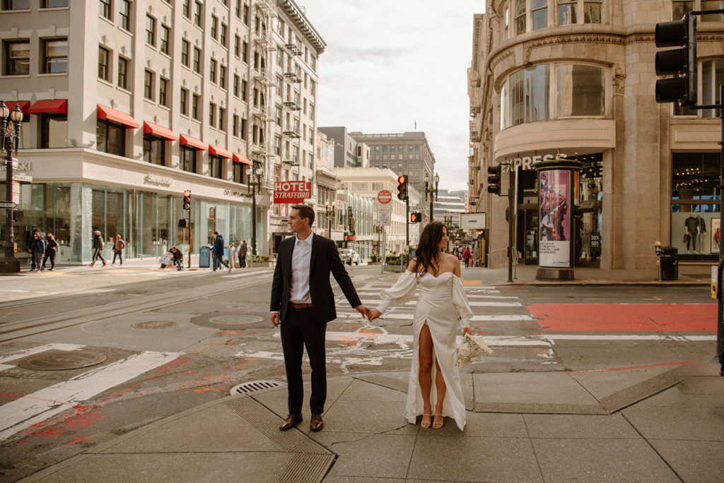 Sydney Jai Photography - San Francisco city elopement, bride and groom holding hands, bride wearing satin off the shoulder wedding dress, groom wearing a classic black suit