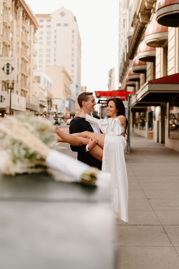 Sydney Jai Photography - San Francisco city elopement, groom holding bride and smiling each other, bride wearing satin off the shoulder wedding dress, groom wearing a classic black suit