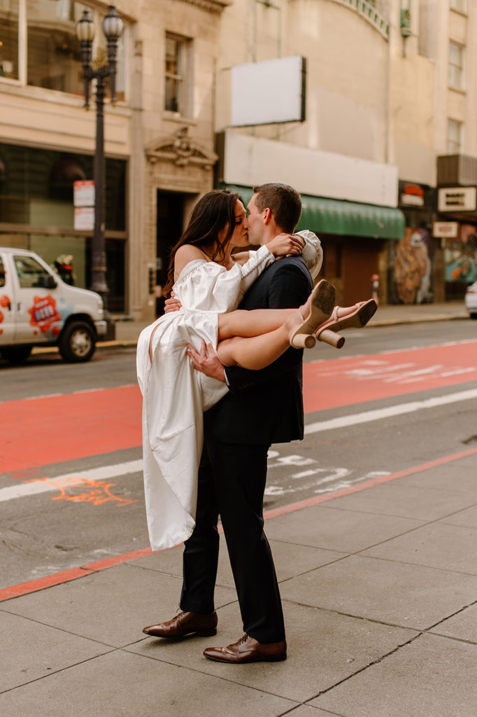 Sydney Jai Photography - San Francisco city elopement, groom holding bride and kissing, bride wearing satin off the shoulder wedding dress, groom wearing a classic black suit