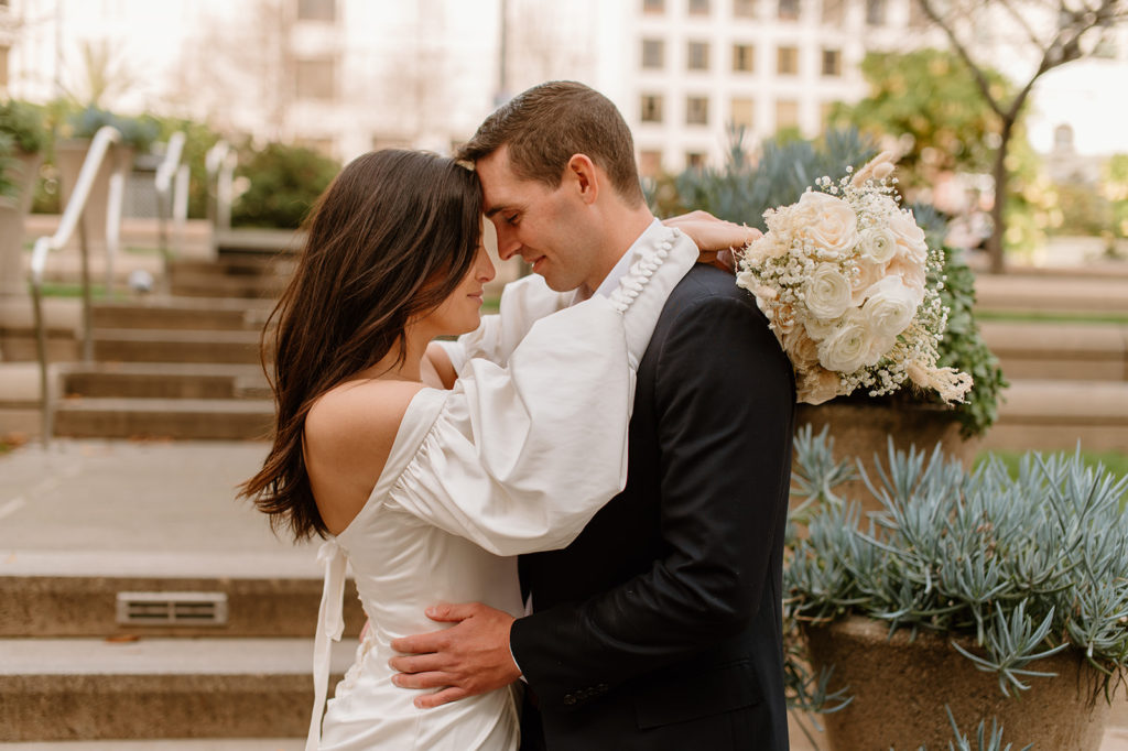 Sydney Jai Photography - San Francisco city elopement, bride and groom holding each other, bride wearing satin off the shoulder wedding dress, groom wearing a classic black suit