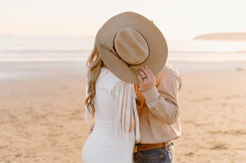 Sydney Jai Photography - Western beach elopement, bride and groom kissing behind cowboy hat